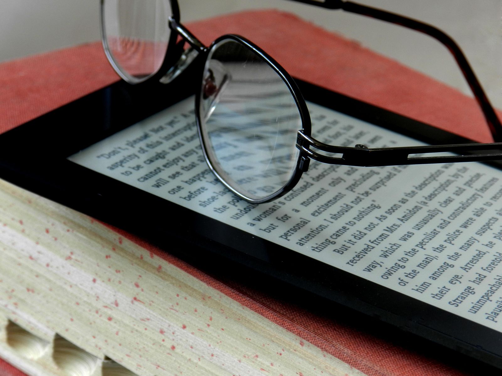 Reading glasses resting on an e-reader beside a printed book